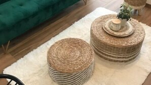 A modern living room with a green sofa, a white throw blanket, and two woven ottomans on a white furry rug. - ''dolmen'' (Plobannalec-Lesconil)