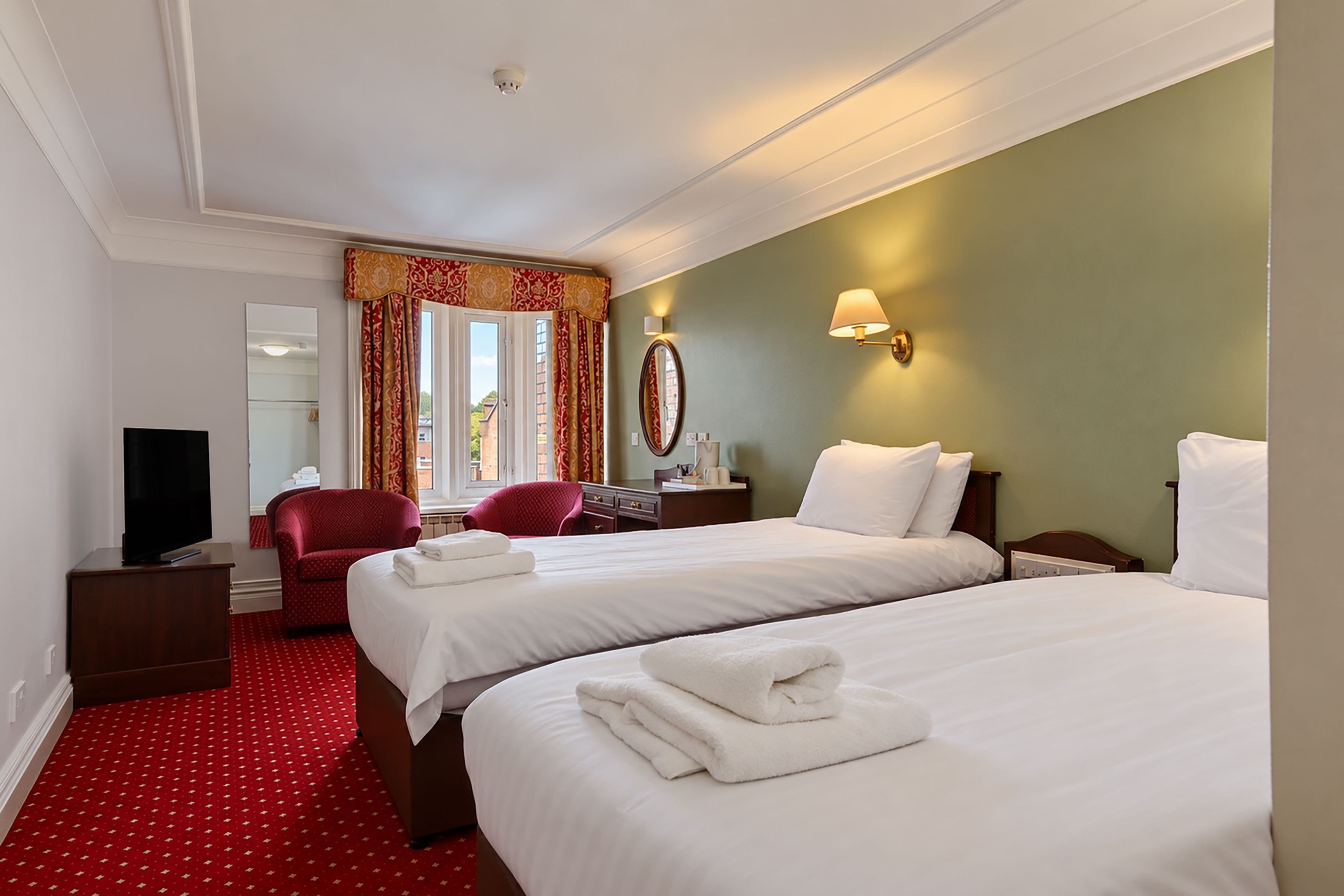 A hotel room with two beds, a TV, a desk, a chair, and a window with curtains.