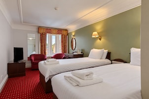Habitación de hotel con dos camas, televisión, escritorio, silla y ventana con cortinas.