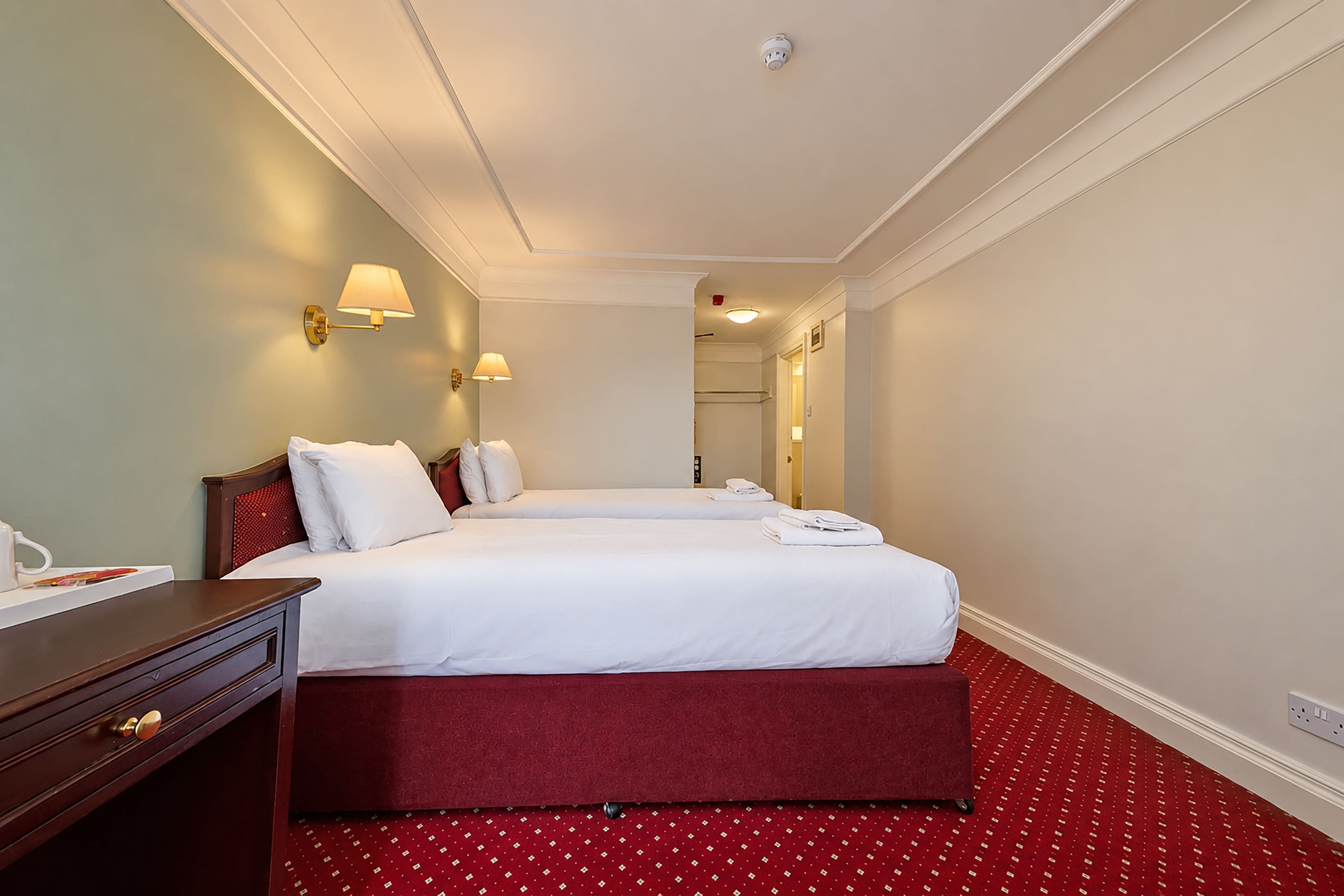 A hotel room with a double bed, a bedside table, and a lamp.