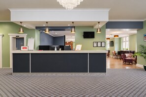 A reception area with a counter, a television mounted on the wall, and a seating area with chairs and a table. - Belvilla Crewe Arms Hotel (Crewe)