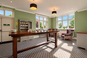 A kitchen with a wooden table, a push bar door, and a window with a view of greenery. - Belvilla Crewe Arms Hotel (Crewe)