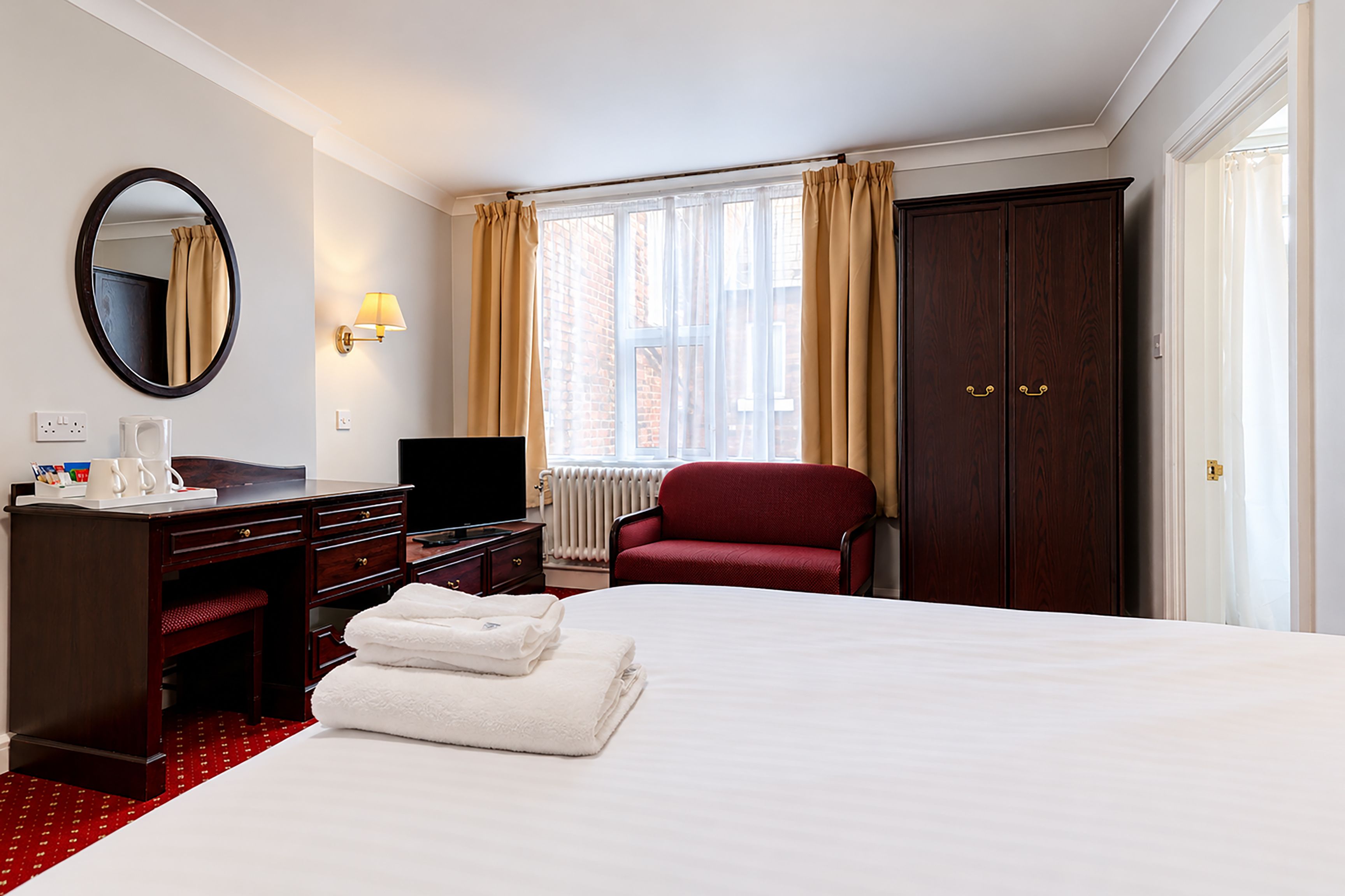 A hotel room with a bed, a desk, a chair, a TV, a wardrobe, and a window with curtains.