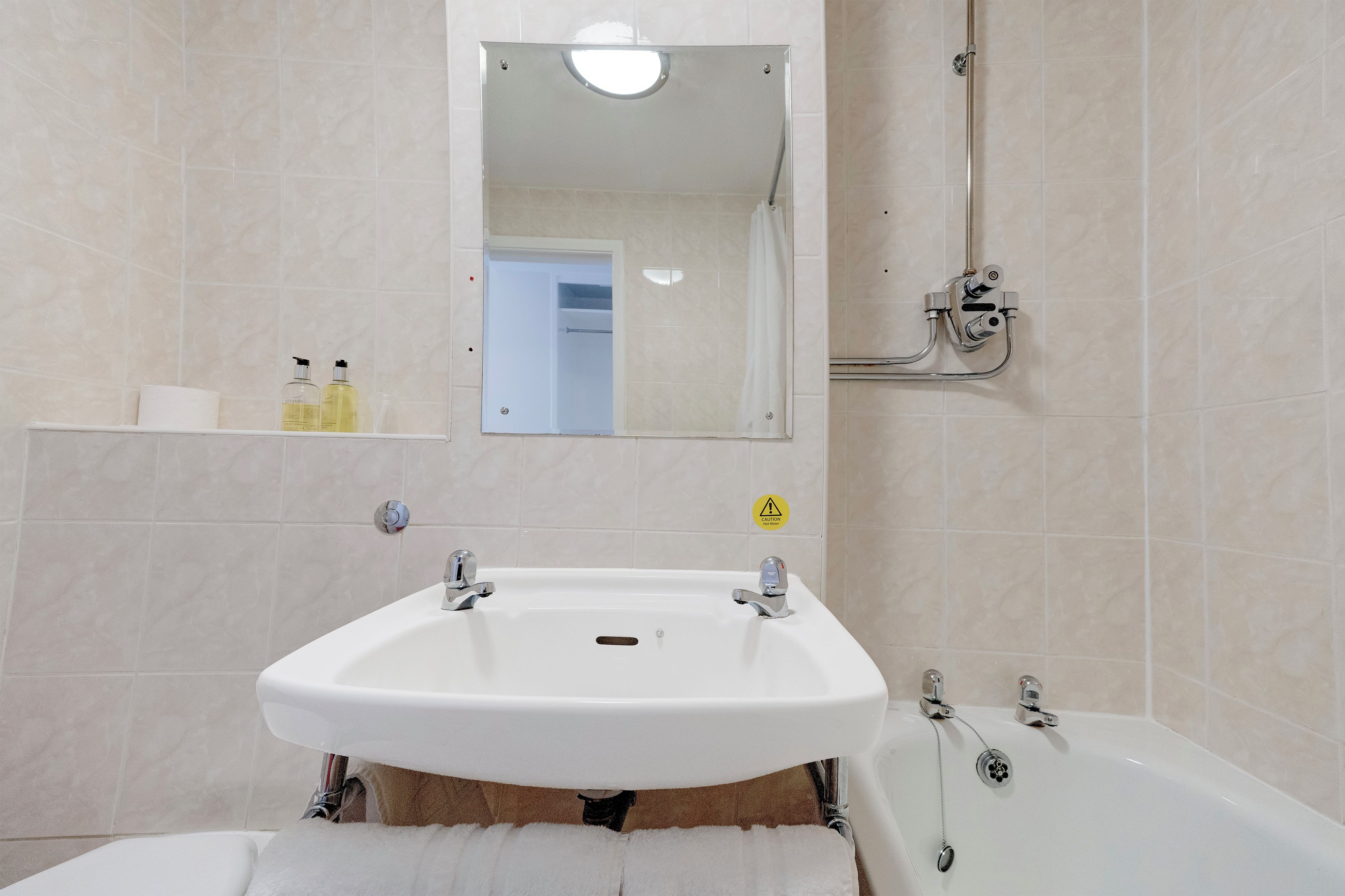 A bathroom with a white sink, a bathtub, and a shower. There is a mirror above the sink and a caution sign on the wall.