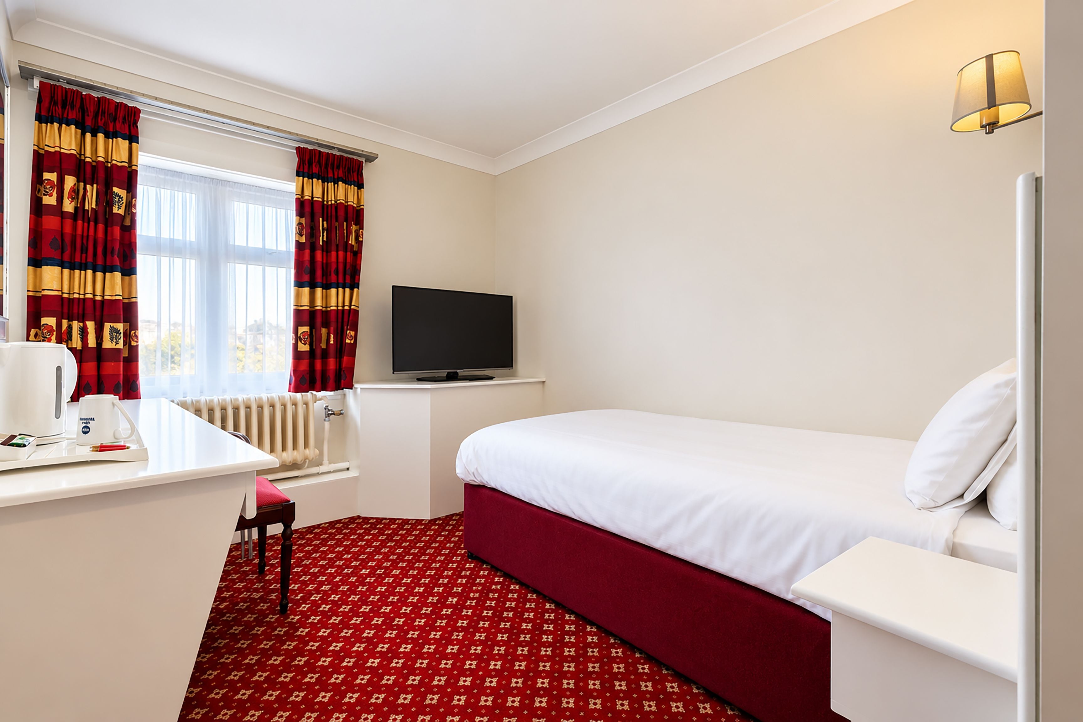 Una camera d'albergo con un letto, una TV, una scrivania con una macchina per il caffè e una finestra con tende.