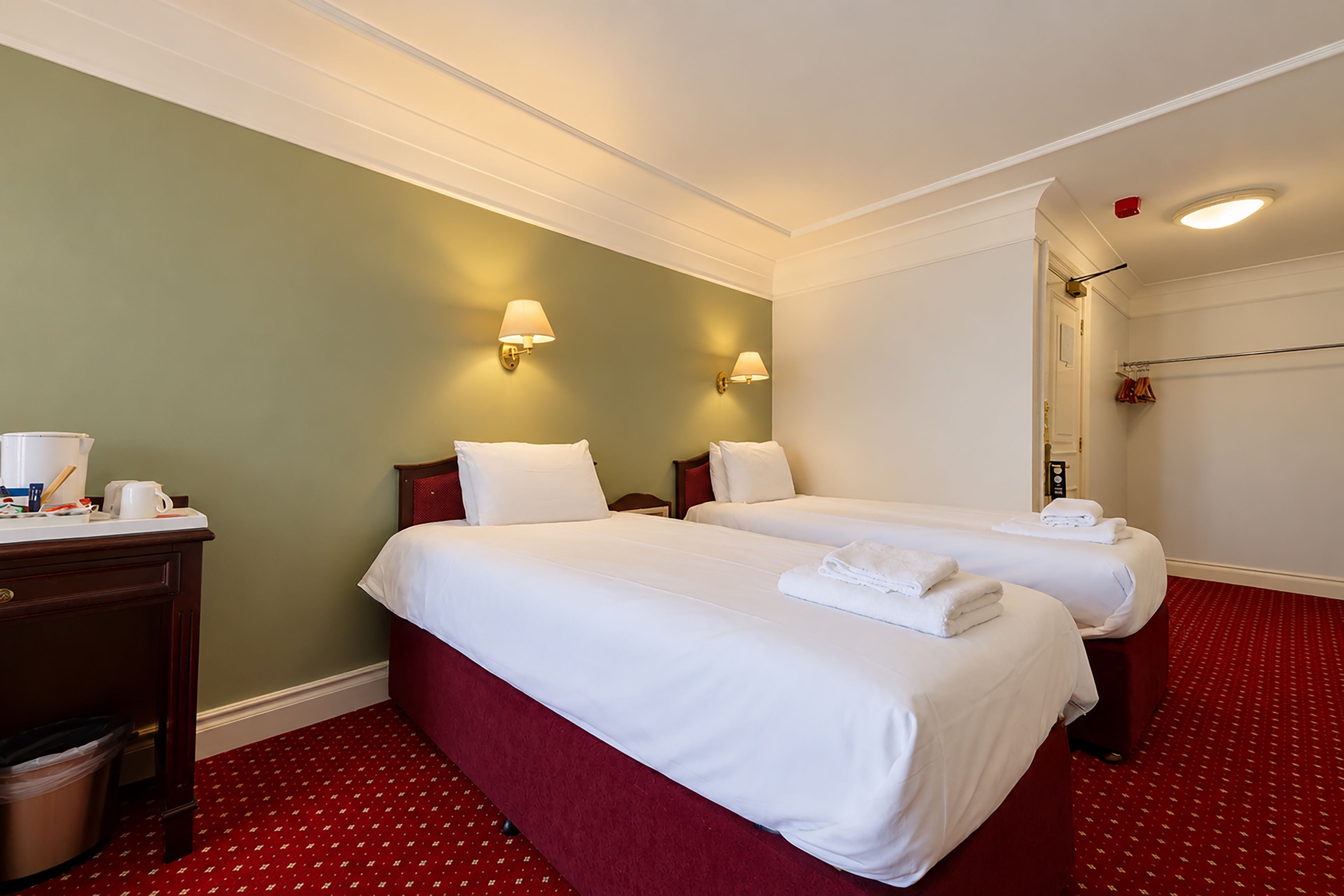 A hotel room with two beds, a desk, and a red carpet.