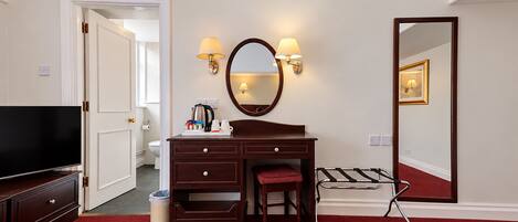 A hotel room with a large bed, a desk with a mirror, a television, and a red carpet.