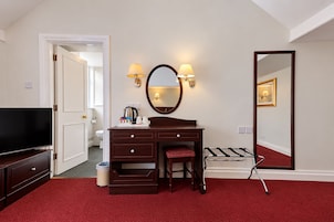 Habitación de hotel con una cama grande, un escritorio con espejo, una televisión y una alfombra roja.