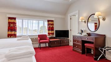 A hotel room with a bed, a desk with a chair, a television, a mirror, and a red carpet.