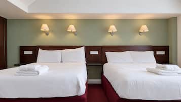 A hotel room with two beds, each with white linens and a neatly folded towel. There are wall-mounted lamps above each bed.