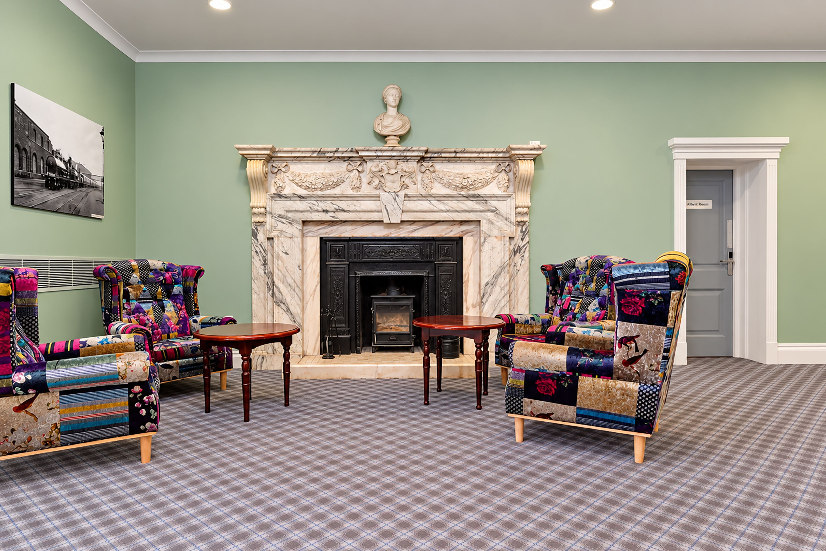Una habitación con chimenea, dos sillones, una mesita y una puerta con la leyenda 'Albert Room'.