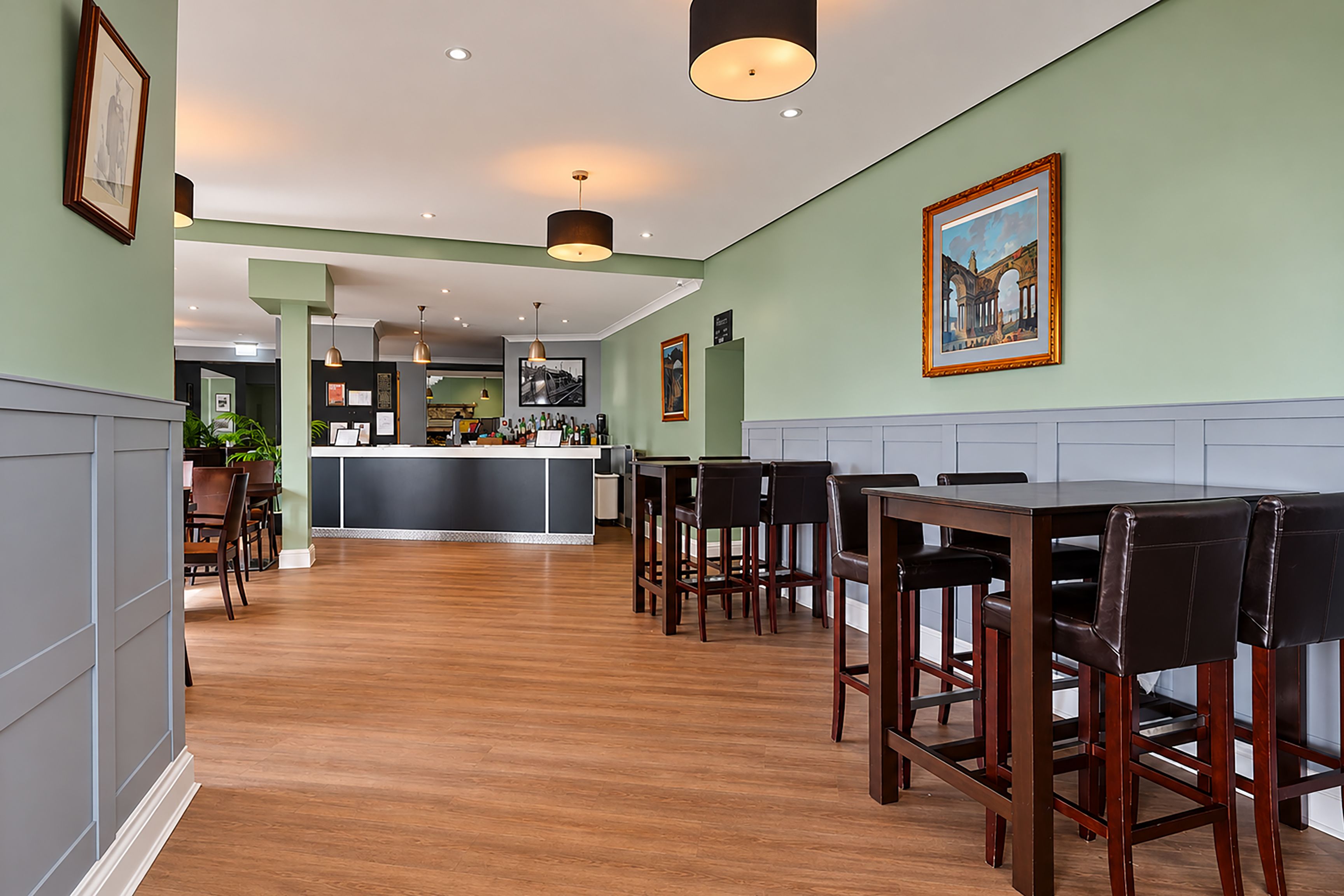 Eine Hotelhalle mit Barbereich, Holzboden und gerahmten Kunstwerken an den Wänden.
