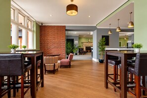A spacious lounge area with a brick wall, wooden flooring, and a fireplace. - Belvilla Crewe Arms Hotel (Crewe)