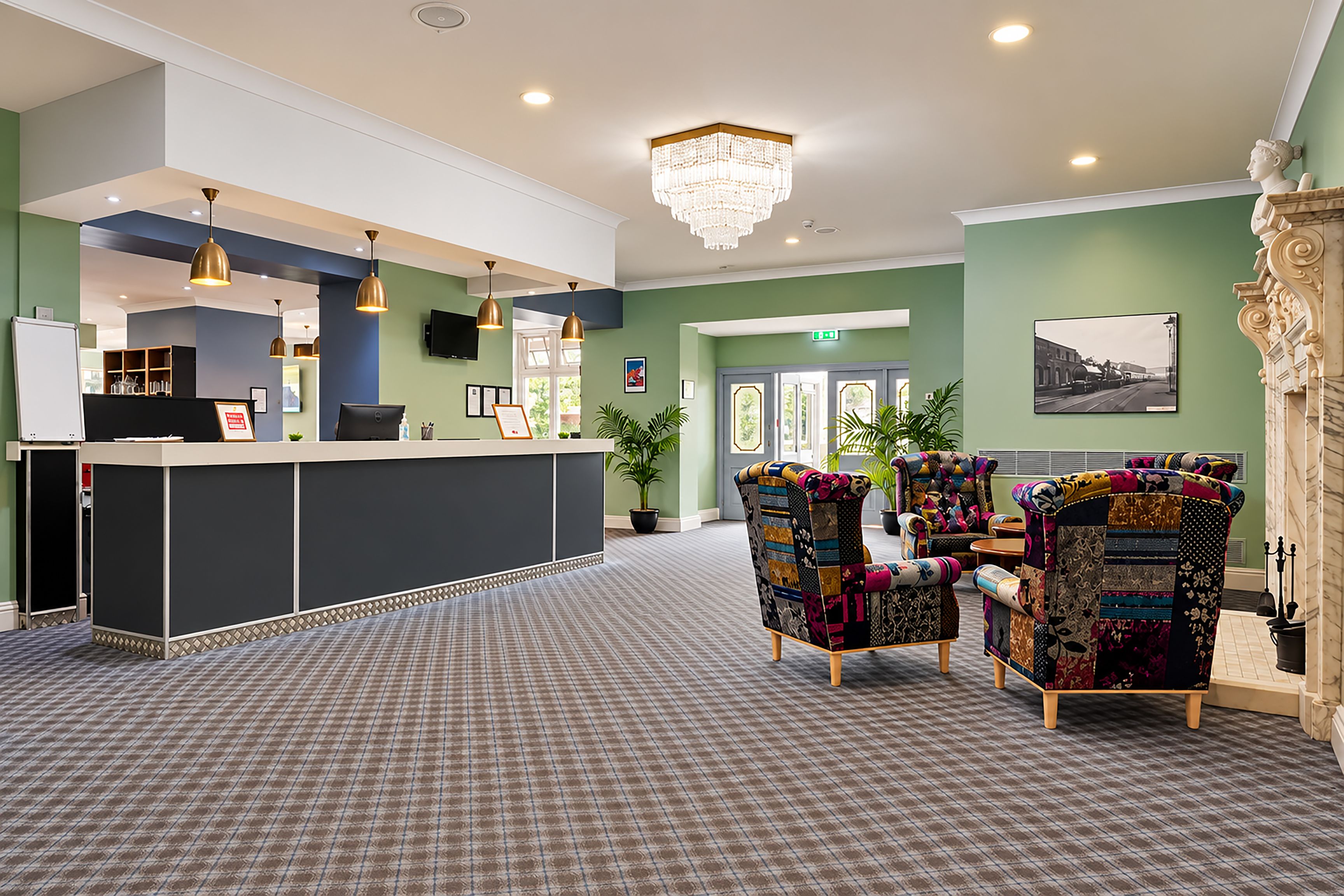 A reception area with a check-in counter, a chandelier, and two patterned armchairs.