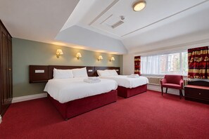 A hotel room with two beds, a red carpet, a red chair, and a window with curtains. - Belvilla Crewe Arms Hotel (Crewe)