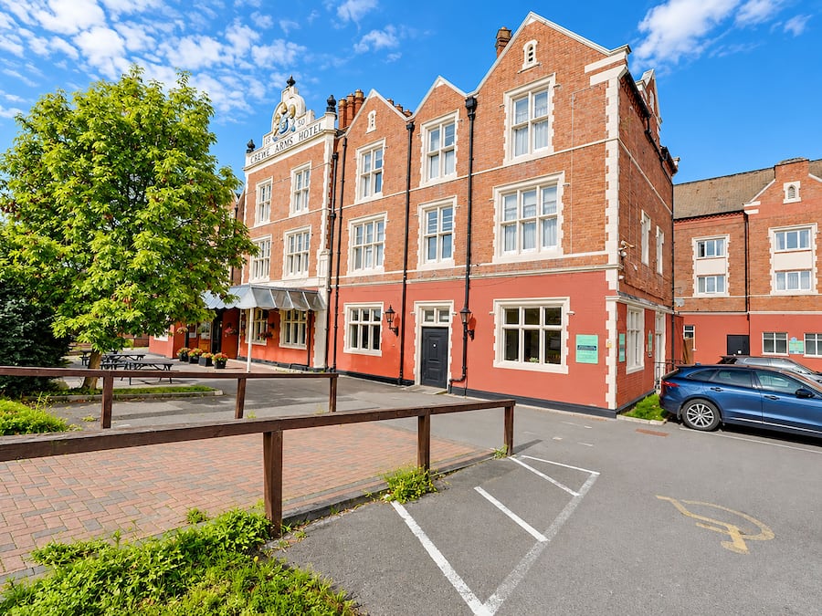 A red-brick building with a sign reading 'CRICKET ARMS HOTEL' and a parking area with a blue car.