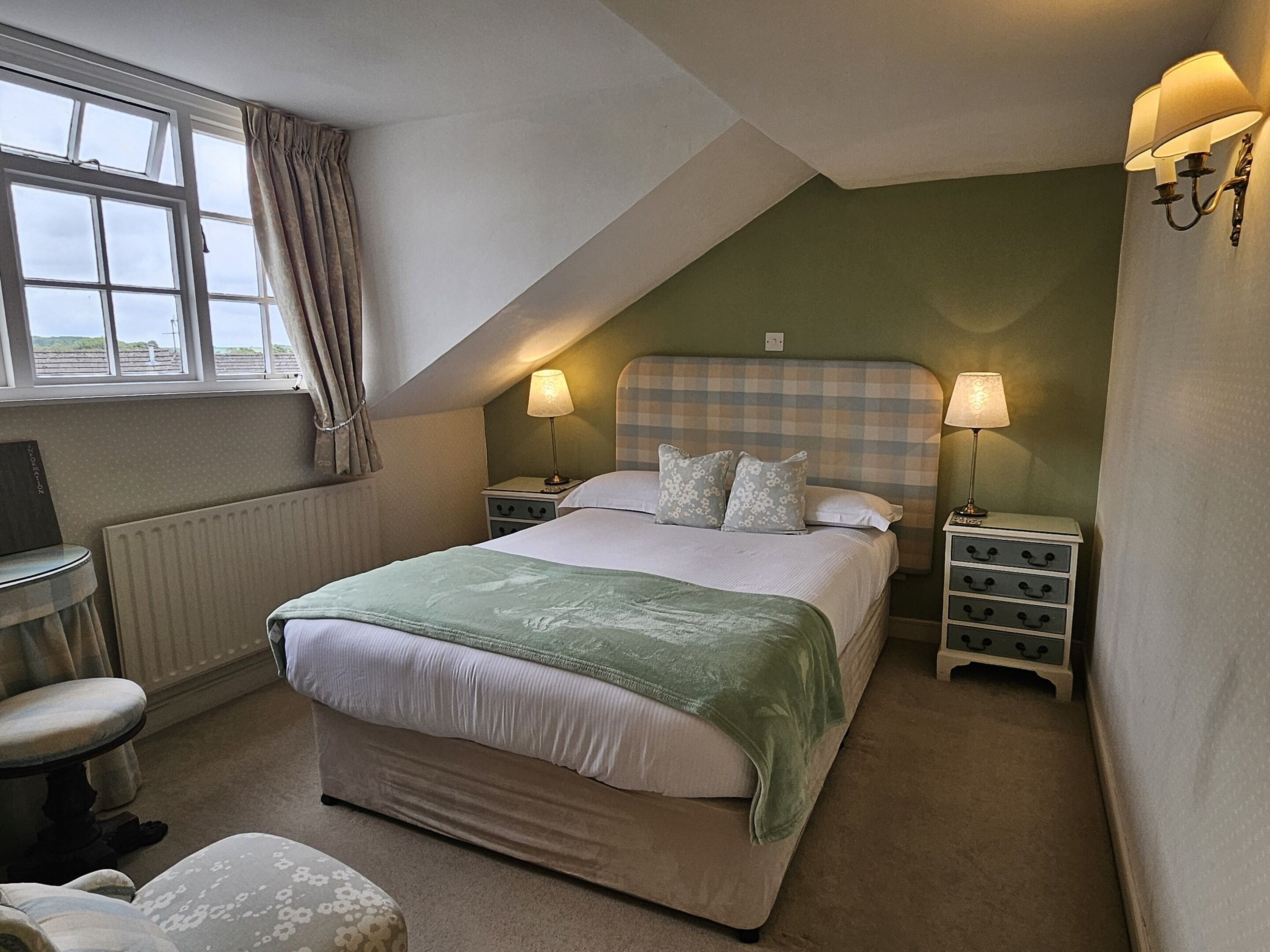 Une chambre à coucher avec un grand lit, deux tables de chevet avec des lampes, une chaise, un radiateur et une fenêtre avec des rideaux.