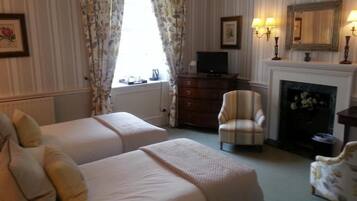 A hotel room with two beds, a television, a fireplace, and a chair.