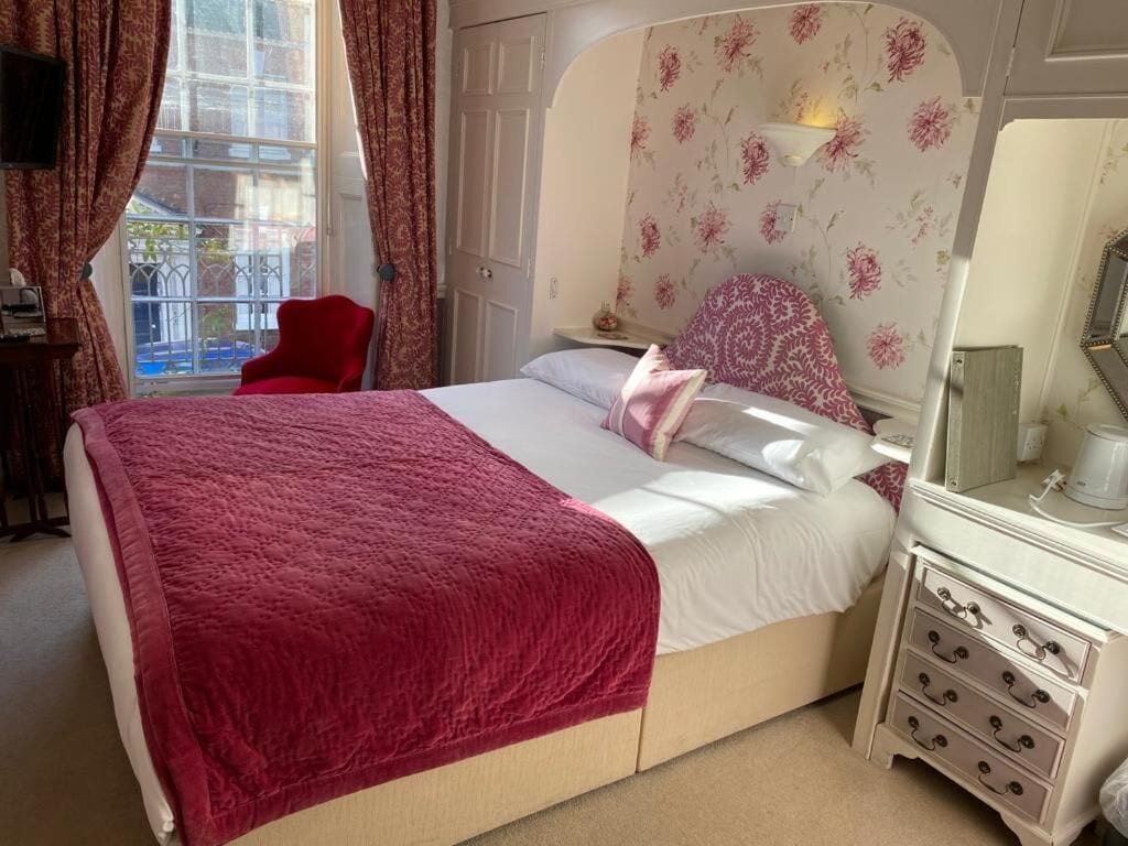 A bedroom with a bed, a dresser, a chair, and a window with curtains.