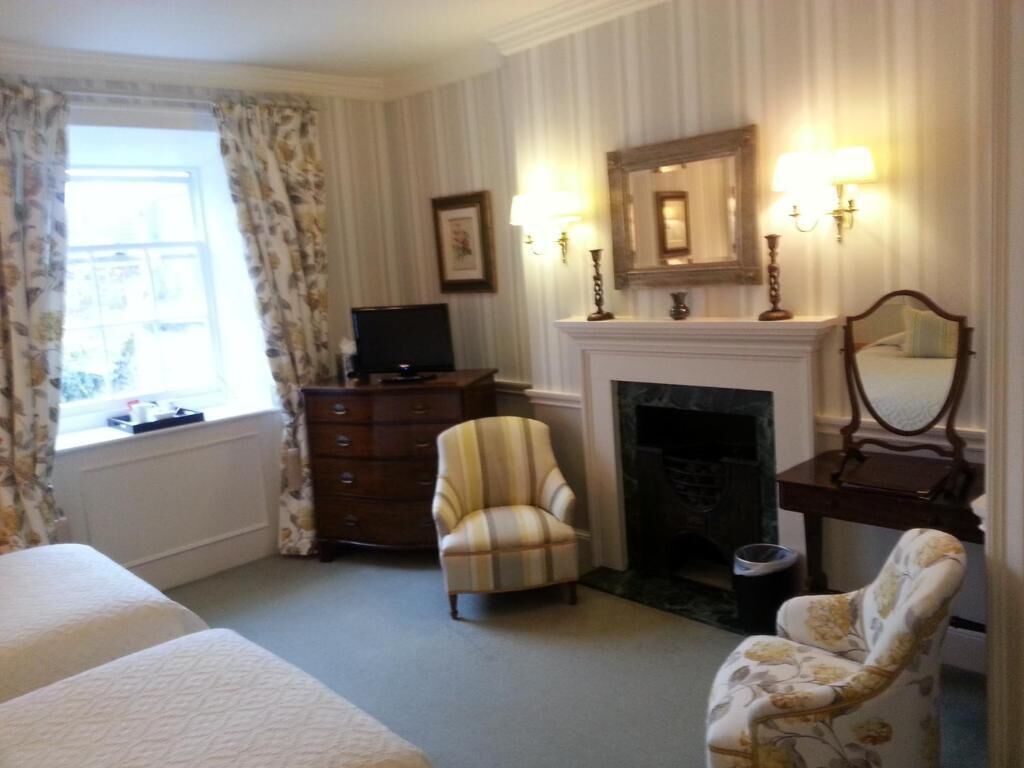 A hotel room with a bed, a dresser, a chair, a fireplace, and a mirror.