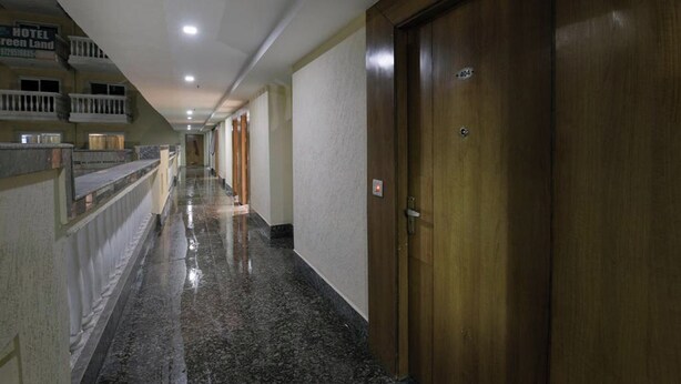 A hotel corridor with a wooden door on the right, a reception area with a balcony on the left, and a marble floor. - Hotel Lotus Paradise (Sonepat)