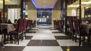 A restaurant with a checkered floor, red chairs, and a glass partition. - Hotel Lotus Paradise (Sonepat)