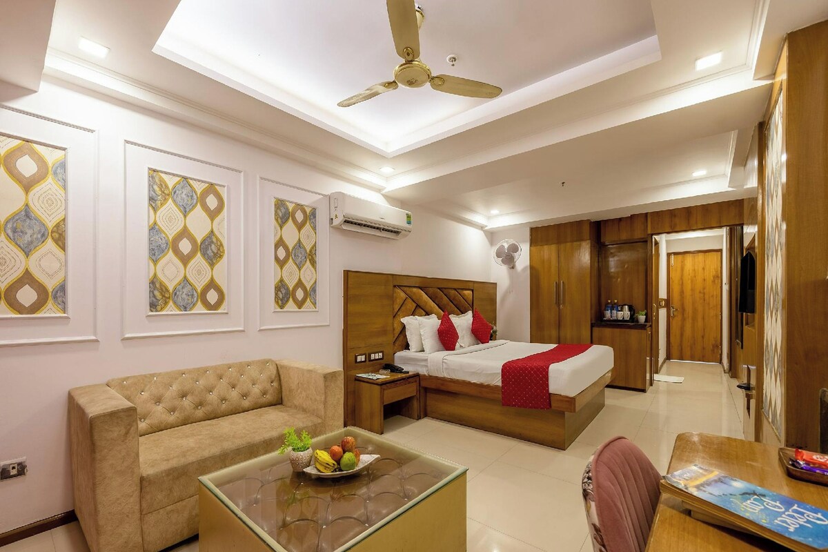 A hotel room with a bed, a sofa, a coffee table with fruit, a fan, and a wardrobe.