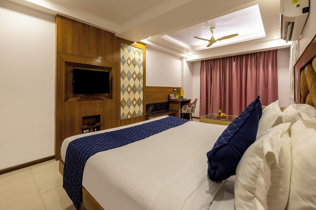 A hotel room with a bed, a TV mounted on the wall, a ceiling fan, and a window with curtains.
