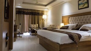 A hotel room with a large bed, a headboard, a desk, a chair, a lamp, and a painting on the wall. - Hotel Lotus Paradise (Sonepat)
