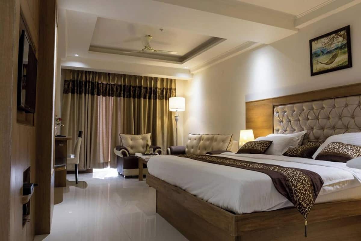 A hotel room with a large bed, a headboard, a desk, a chair, a lamp, and a painting on the wall.