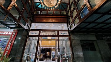 The entrance to Hotel Lotus with a grand chandelier, glass doors, and a visible interior pathway leading inside.
