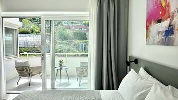 Habitación de hotel con cama, balcón con silla y mesa, y un cuadro en la pared.
