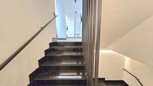 A modern staircase with black steps and a glass railing, leading to a bright hallway. - A&A Rooms (Anacapri)