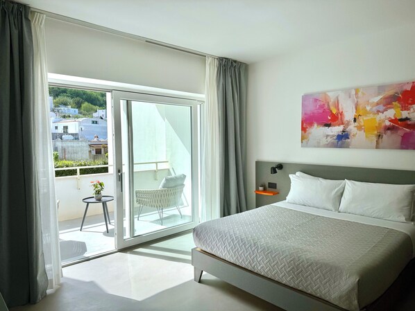 Una habitación de hotel moderna con una cama grande, un balcón con una silla y un cuadro abstracto y colorido en la pared.