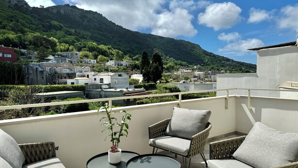 A balcony with wicker furniture, a small table, and a potted plant. - A&A Rooms (Anacapri)