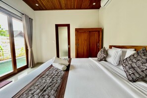A hotel room with a large bed, a wooden wardrobe, and a sliding glass door leading to a pool area. - Belvilla Pantai Senja Resort Central Ubud (Pecatu)