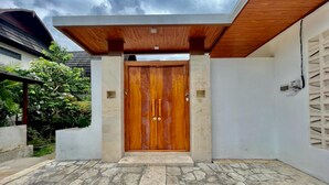 A modern house with a wooden double door, stone flooring, and a covered entrance. - Belvilla Pantai Senja Resort Central Ubud (Pecatu)