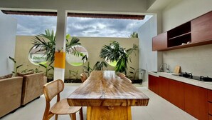 A modern kitchen with a wooden dining table, built-in cabinets, and a view of the outdoors. - Belvilla Pantai Senja Resort Central Ubud (Pecatu)