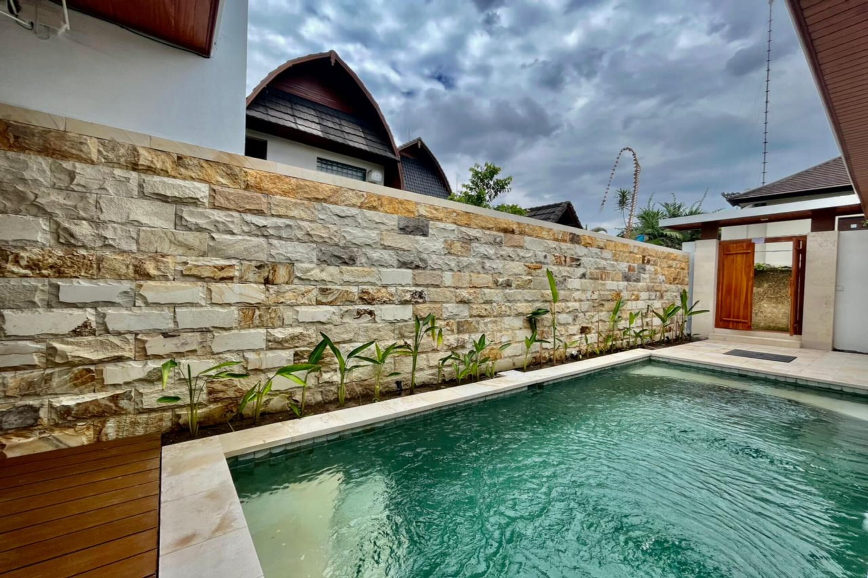 Una piscina con pared de piedra, muelle de madera y vistas a edificios cercanos.