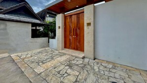 A modern house with a large wooden door, stone flooring, and a covered patio area. - Belvilla Pantai Senja Resort Central Ubud (Pecatu)