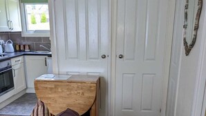 Une cuisine compacte avec des meubles blancs, une table en bois et un canapé marron agrémenté de coussins à rayures.