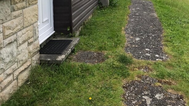 Une rangée d’immeubles à deux étages, dotés de fondations en pierre, d’un trottoir pavé et d’un arbre aux feuilles rouges en arrière-plan.