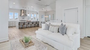A spacious living room with a white sofa, a dining area with chairs, and a kitchen with a large island. - Pet-Friendly Home@Cinnamon Shore South w/ Gulf View & Extras Galore! (Port Aransas)