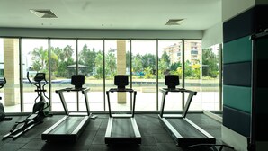 Ett gym med löpband och annan träningsutrustning, stora fönster med utsikt över palmer och byggnader.