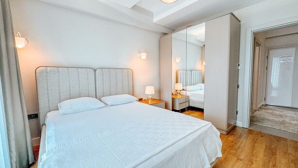 Ett hotellrum med en stor säng, två sängbord med lampor, en spegel och en dörr.