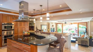 A modern kitchen with stainless steel appliances, a central island, and a dining area with wicker furniture.