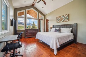 Un dormitorio con una cama grande, un escritorio y una silla. Varias ventanas ofrecen vistas a montañas.