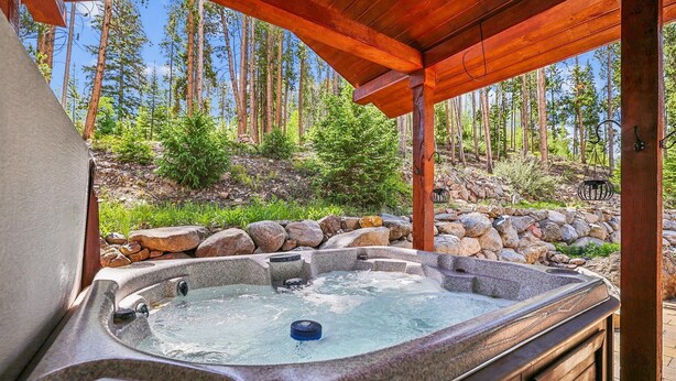Un jacuzzi bajo una pérgola de madera con un bosque de fondo.