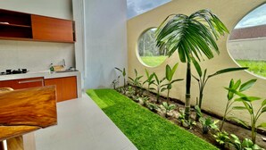A modern kitchen with built-in cabinets, a dining area with a wooden table, and a small indoor garden with plants and a circular window. - Belvilla Tirta Sari Resort Central Ubud (Ubud)