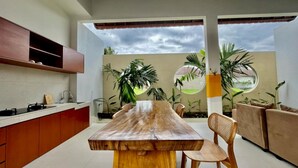 A modern kitchen with a wooden dining table, built-in cabinets, and a large window overlooking a garden. - Belvilla Tirta Sari Resort Central Ubud (Ubud)